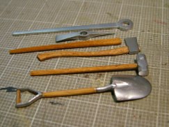The wooden handles were then masked off and the metal parts of the tools were sprayed using Testor's brand buffable metalizer paint. I chose stainless steel and plate aluminum. Once a few light coats were applied I allowed the lacquer based paint to dry thoroughly. Once dry I used a soft cotton rag to buff the finish to a bright sheen. Next will come a layer of darker mettalic grey or gunmetal acrylic paint. Once that is painted on I will be able to "rub through" the acrilic paint exposing the brighter color underneath making it look the metal in worn and shiny on the edges. Then I will add layers of green and whitewash paint to represent field applied paint that will also be worn through.